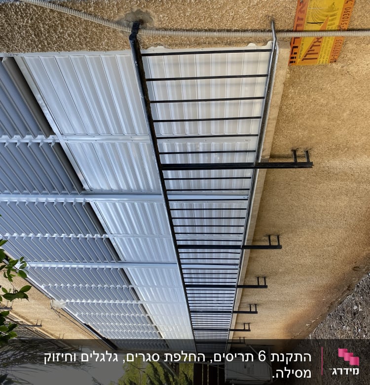 תריסים לבנים מותקנים על קיר חיצוני עם מסגרת מתכת.